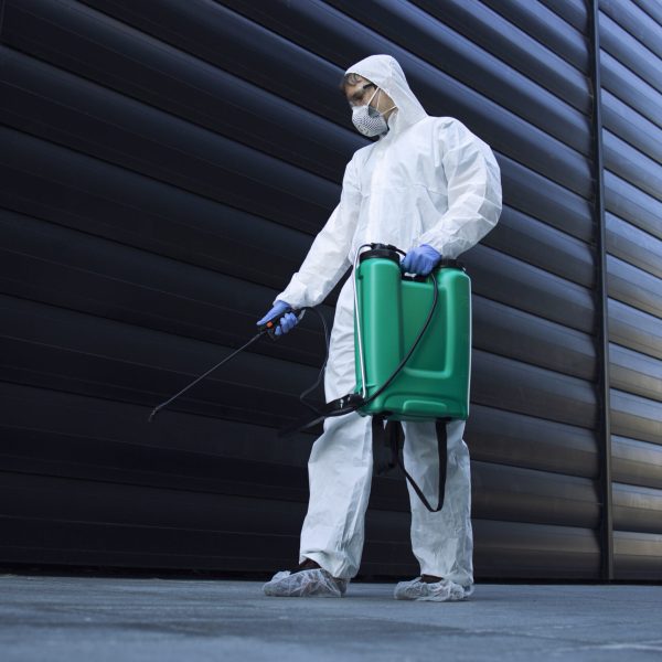 Person in white chemical protection suit doing disinfection of public areas to stop spreading highly contagious corona virus.